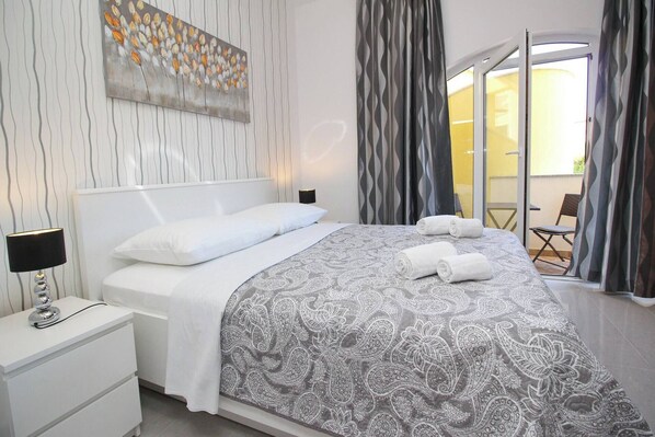 Een moderne hotelkamer met een groot bed, witte beddengoed, een gestreept plaid, een nachtkastje met een lamp, en uitzicht op de omgeving door een schuifdeur.