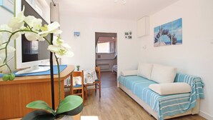 Une pièce avec un bureau en bois, un ordinateur, un canapé recouvert d’un tissu à rayures et un grand pot d’orchidées blanches.