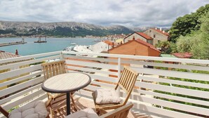 Un balcon avec une table et deux chaises, donnant sur une marina où sont amarrés des bateaux, et sur une ville en arrière-plan.