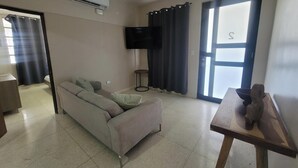 Una sala de estar con un sofá, un televisor, una mesita y una ventana con cortinas.