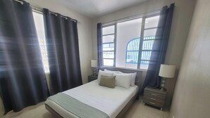 Habitación de hotel con cama, dos mesitas de noche, una ventana con cortinas y vistas al exterior.