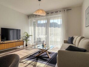 A modern living room with a flat-screen TV, a glass coffee table, a sofa, and a large window with sheer curtains. - Experience Cochem: Moselle view, view of the Reichsburg & old town directly opposite (Cochem)