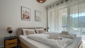Une chambre d’hôtel moderne avec un grand lit, deux tables de chevet, une petite table et une vue sur l’extérieur.