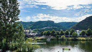 Une vue sur la rivière, avec des voitures garées, un pont piétonnier et des bâtiments en arrière-plan.