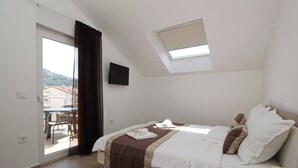 Une chambre avec un lit, une télévision, un balcon et une vue sur les bâtiments environnants.