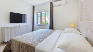A hotel room with a bed, a TV, a window, and an air conditioning unit.