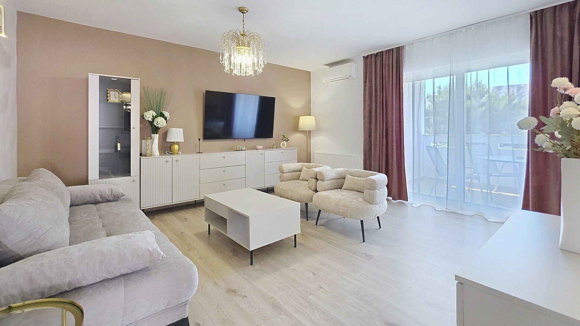 A modern living room with a flat-screen TV, a sofa, a coffee table, and a chandelier.