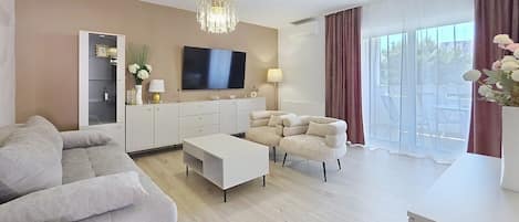 A modern living room with a flat-screen TV, a sofa, a coffee table, and a chandelier.