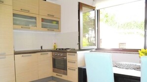 A kitchen with light wooden cabinets, a stove, and a window with a view of greenery. - Apartment Starcevic-Filipovic with a Backyard and BBQ, 150 m from the Beach (Baska)