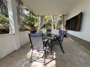 An outdoor patio with a table and chairs, surrounded by curtains and a view of trees.