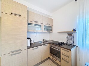 A compact kitchen with light wood cabinets, a stainless steel sink, and a built-in oven.