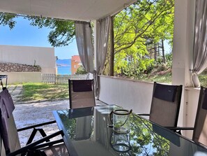 Un pati exterior amb taula i cadires de vidre, i un vas de vidre.