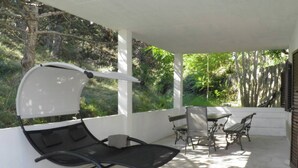 A covered patio with a black lounge chair, a table, and two chairs. - Apartment Starcevic-Filipovic with a Backyard and BBQ, 150 m from the Beach (Baska)