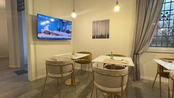 A conference room with a television displaying a news program, a painting on the wall, and a window with curtains.