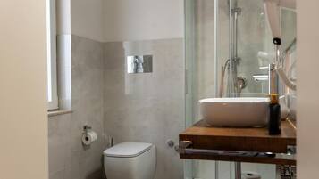 Un baño moderno con cabina de ducha de vidrio, un inodoro y un lavabo con encimera de madera.