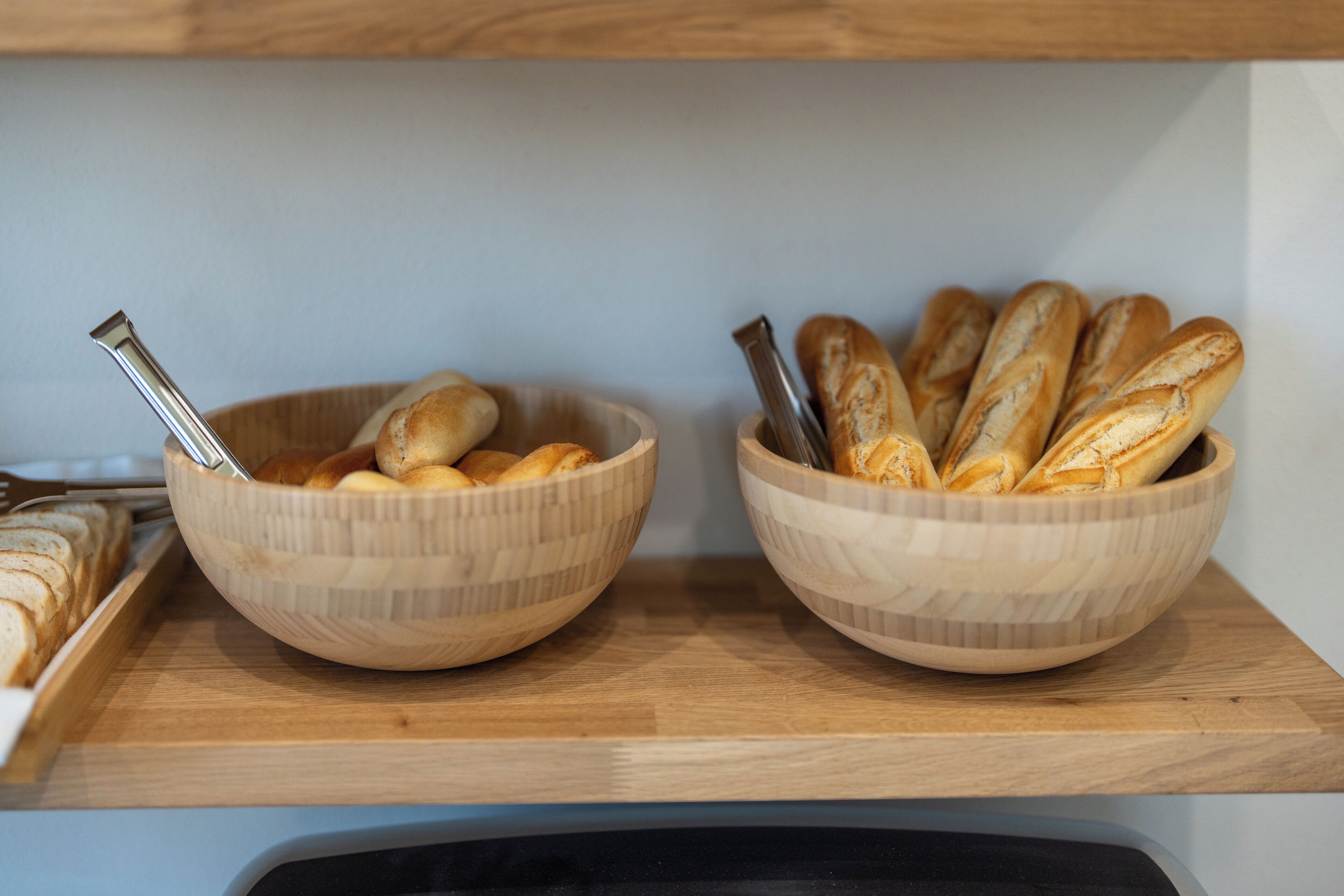 Two wooden bowls on a shelf containing bread.
