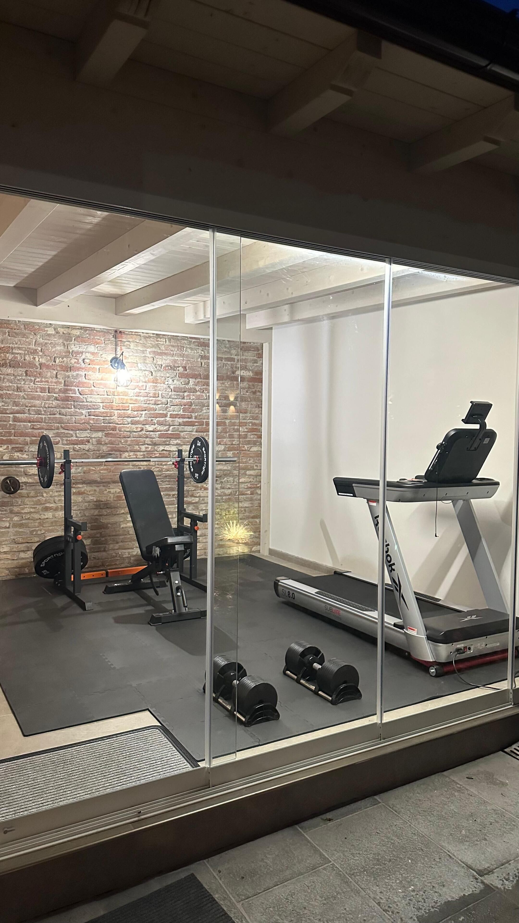 A modern home gym with a brick wall, a bench press, a treadmill, and weight racks.
