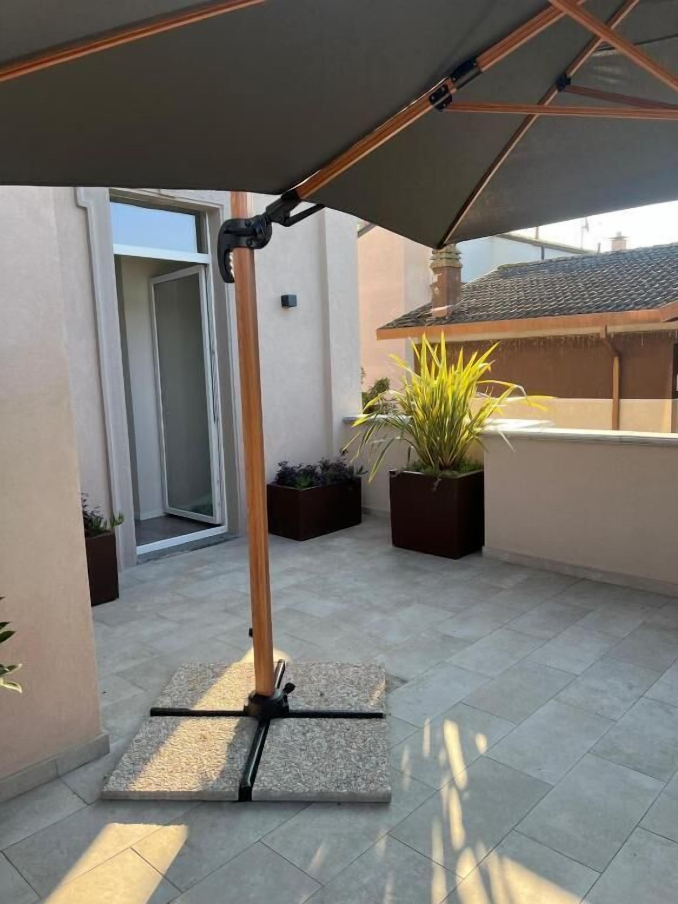 Un'area patio esterna con un ombrellone retrattile, piante in vaso e una porta che dà su un altro ambiente.