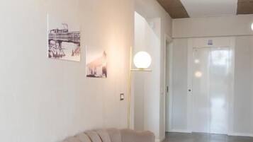 Ein moderner Flur mit einem beigen Sofa, Wandleuchten und einer Tür im Hintergrund.