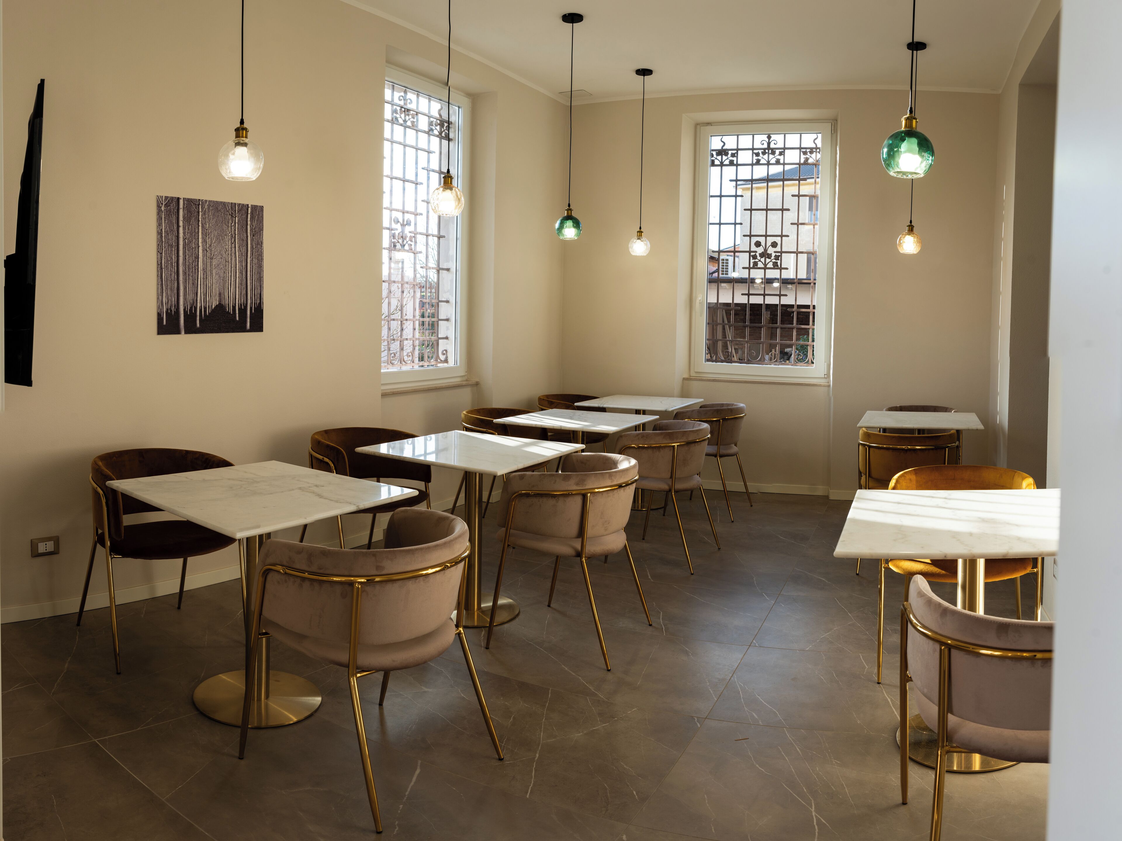 A dining area with tables and chairs, large windows with metal grilles, and hanging pendant lights.