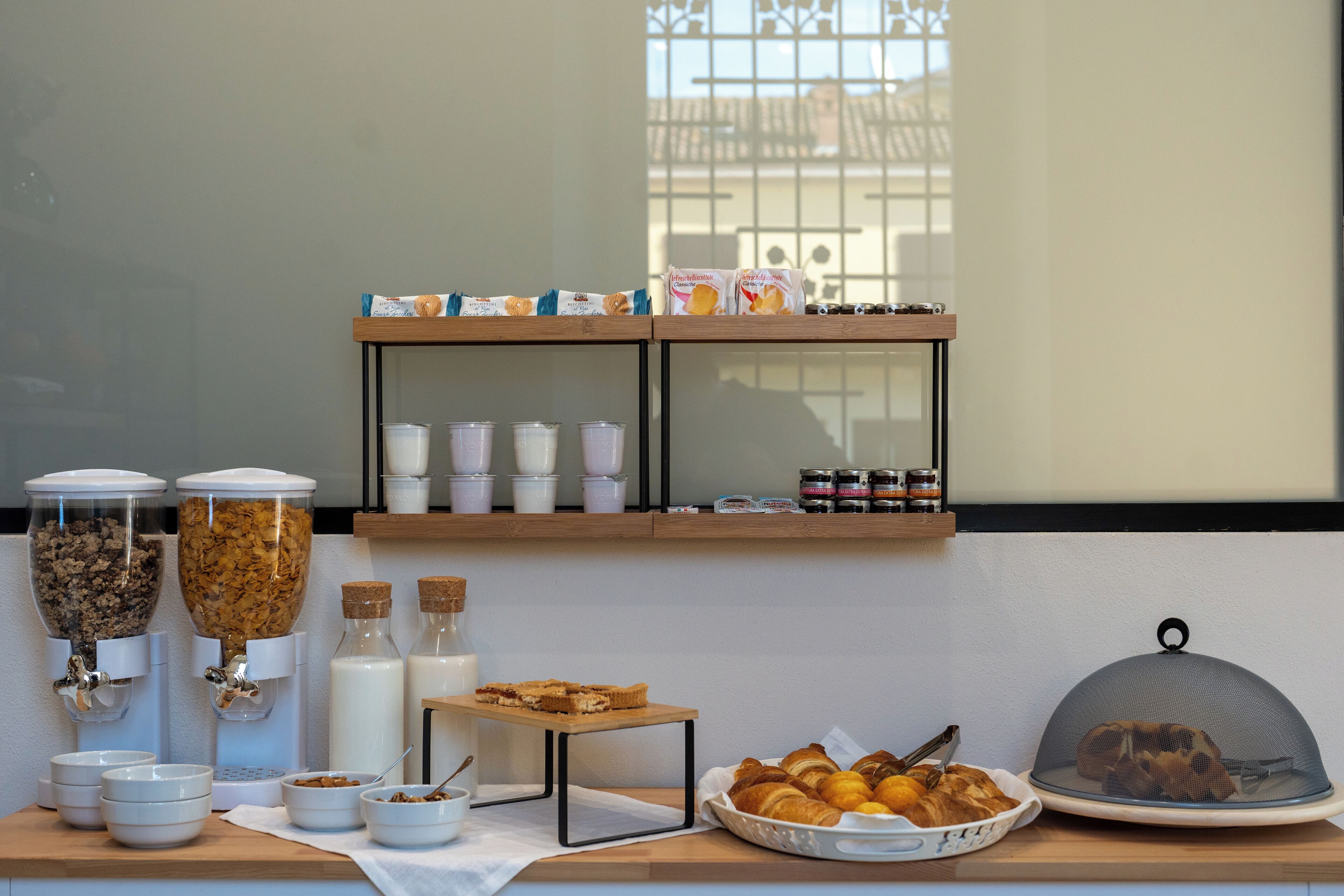 Ein Frühstücksbuffet mit verschiedenen Speisen, darunter Müsli, Milch und Gebäck, auf einer Holztischplatte präsentiert.