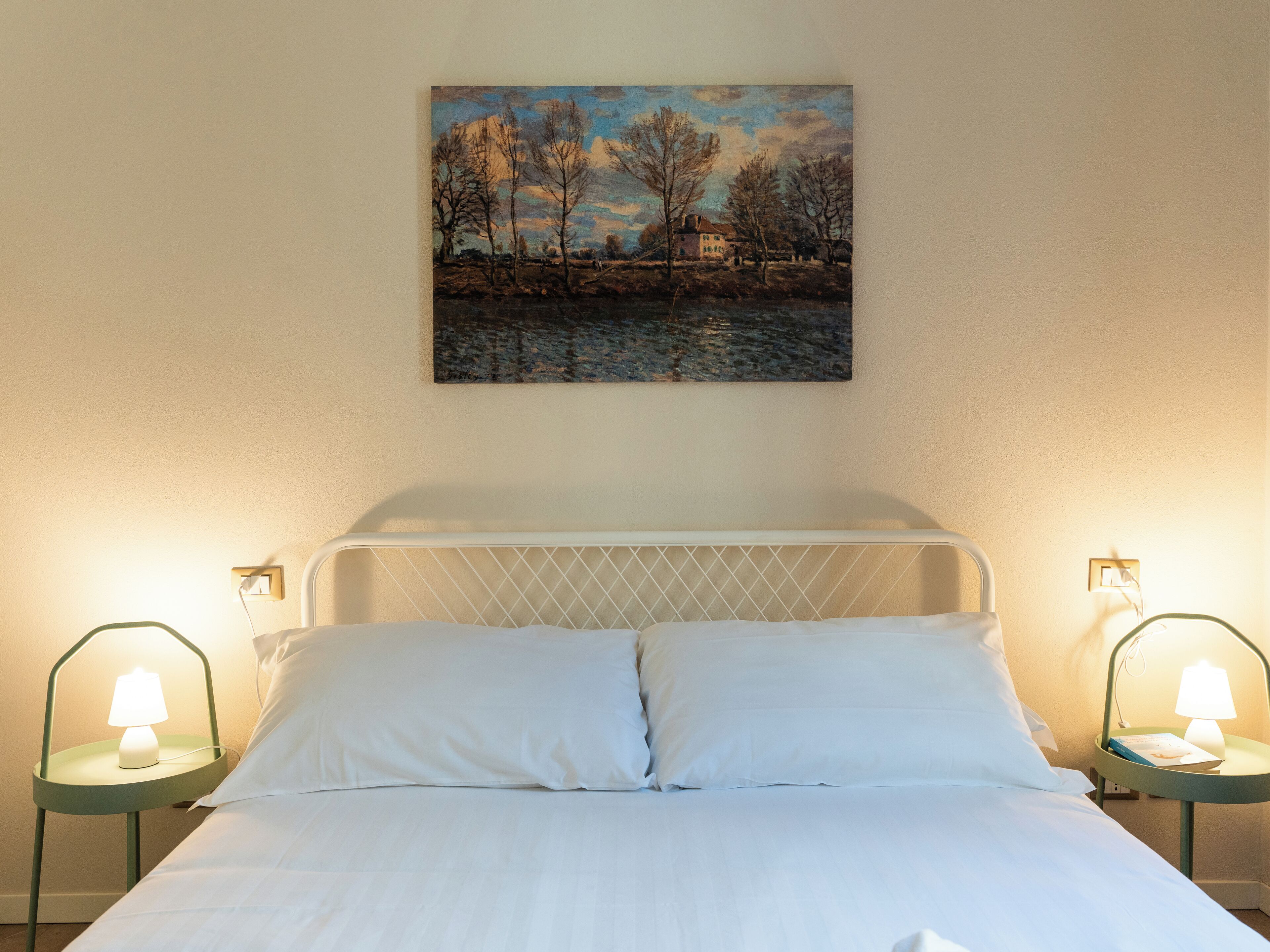 Ein Schlafzimmer mit einem Bett, zwei Nachttischen mit Lampen und einem Gemälde an der Wand.