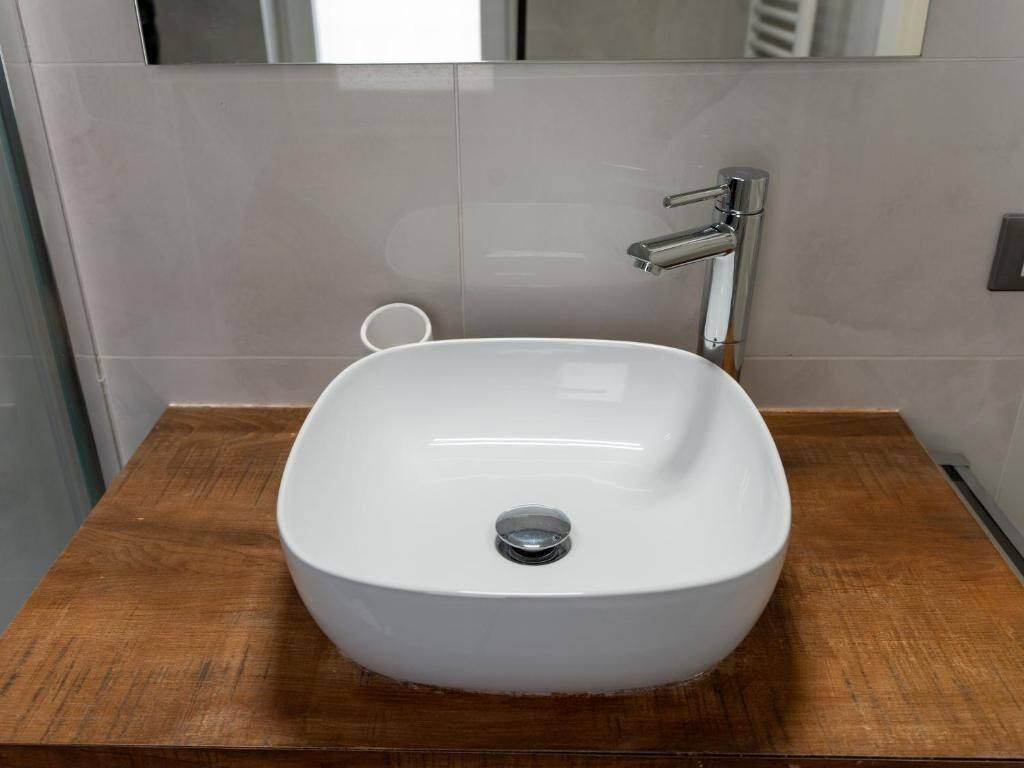 A bathroom with a white sink, a chrome faucet, and a wooden countertop.