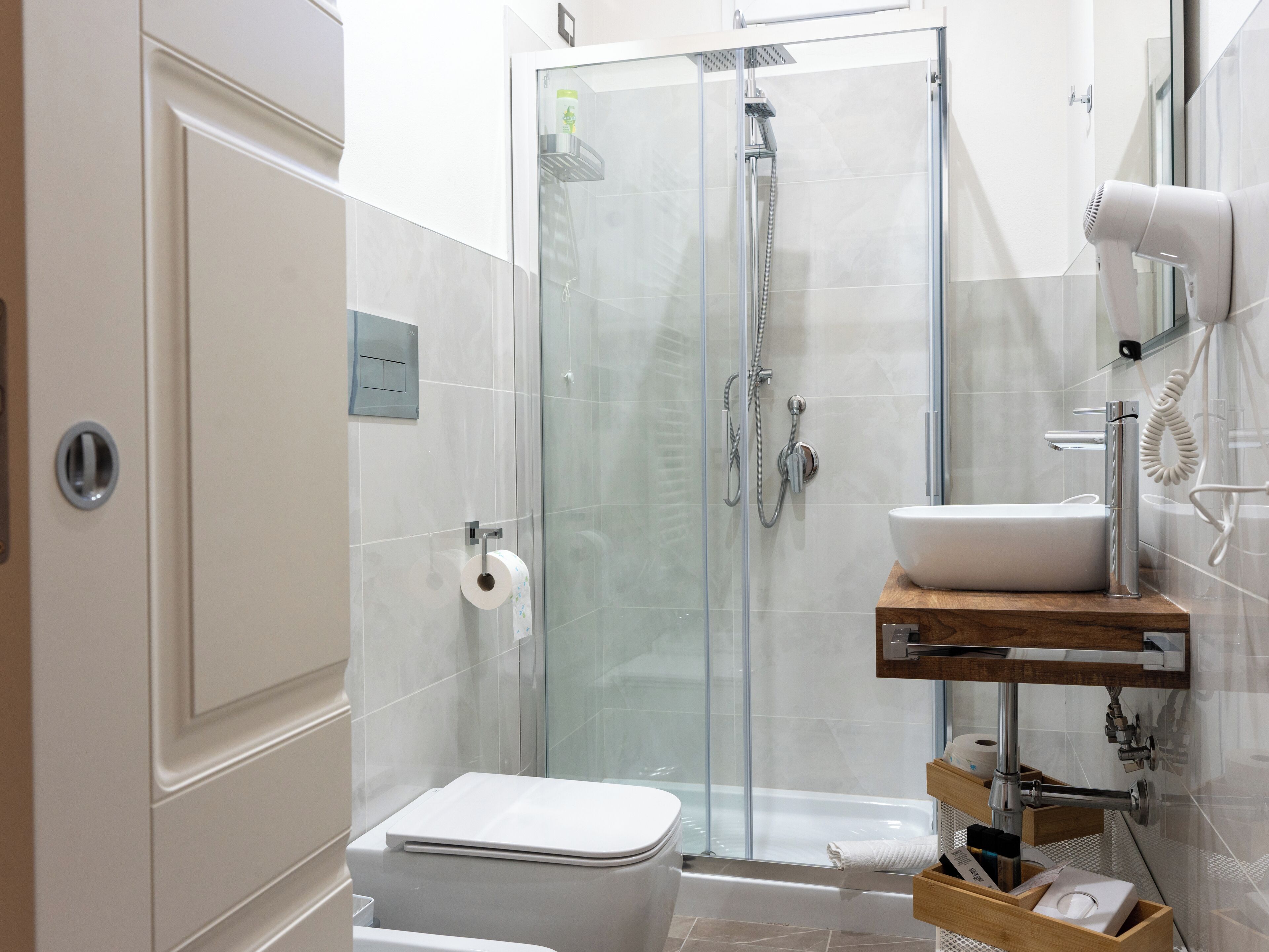 Un baño moderno con cabina de ducha de vidrio, inodoro blanco y tocador de madera con lavabo.