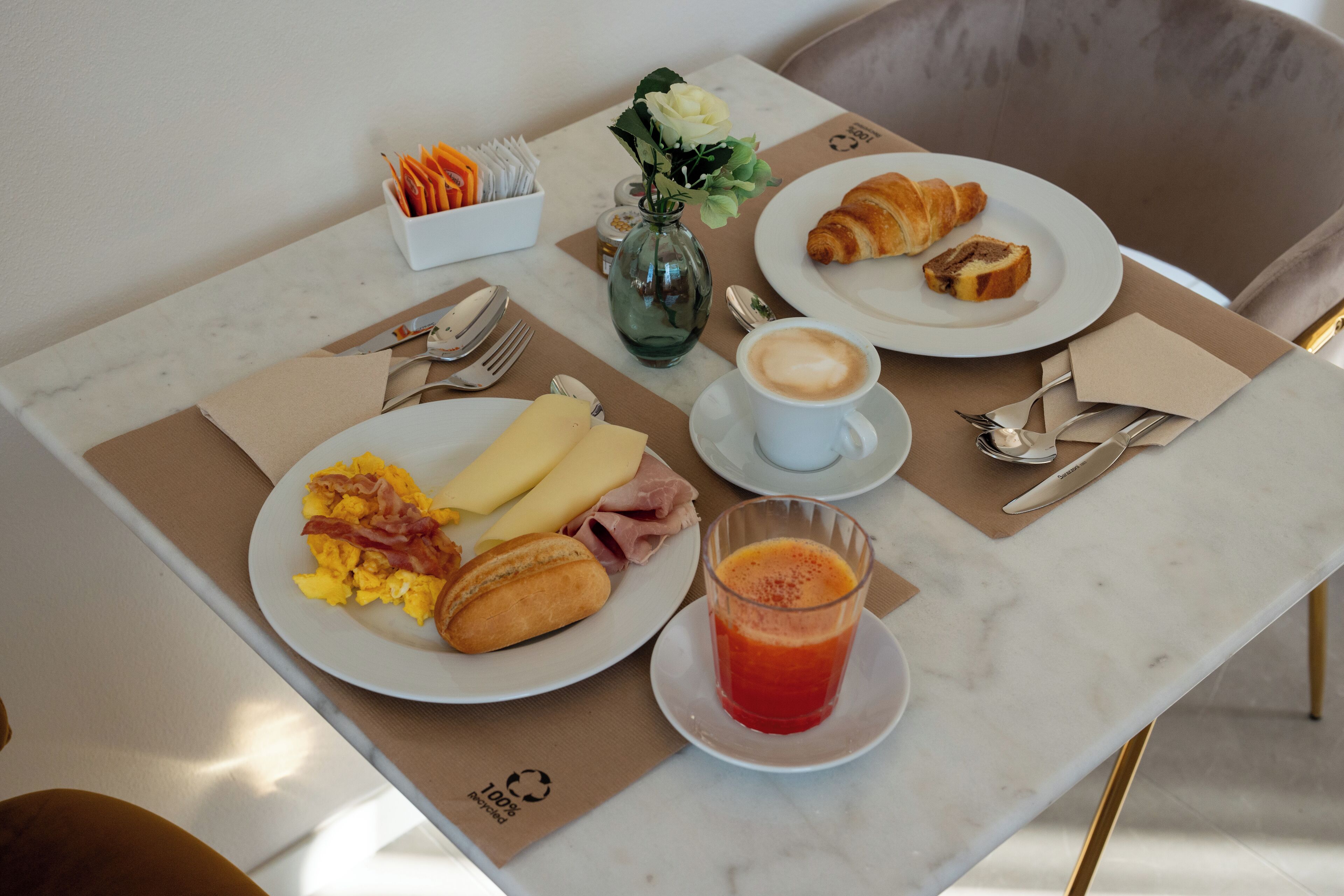 A breakfast table with croissants, scrambled eggs, ham, and a glass of orange juice.