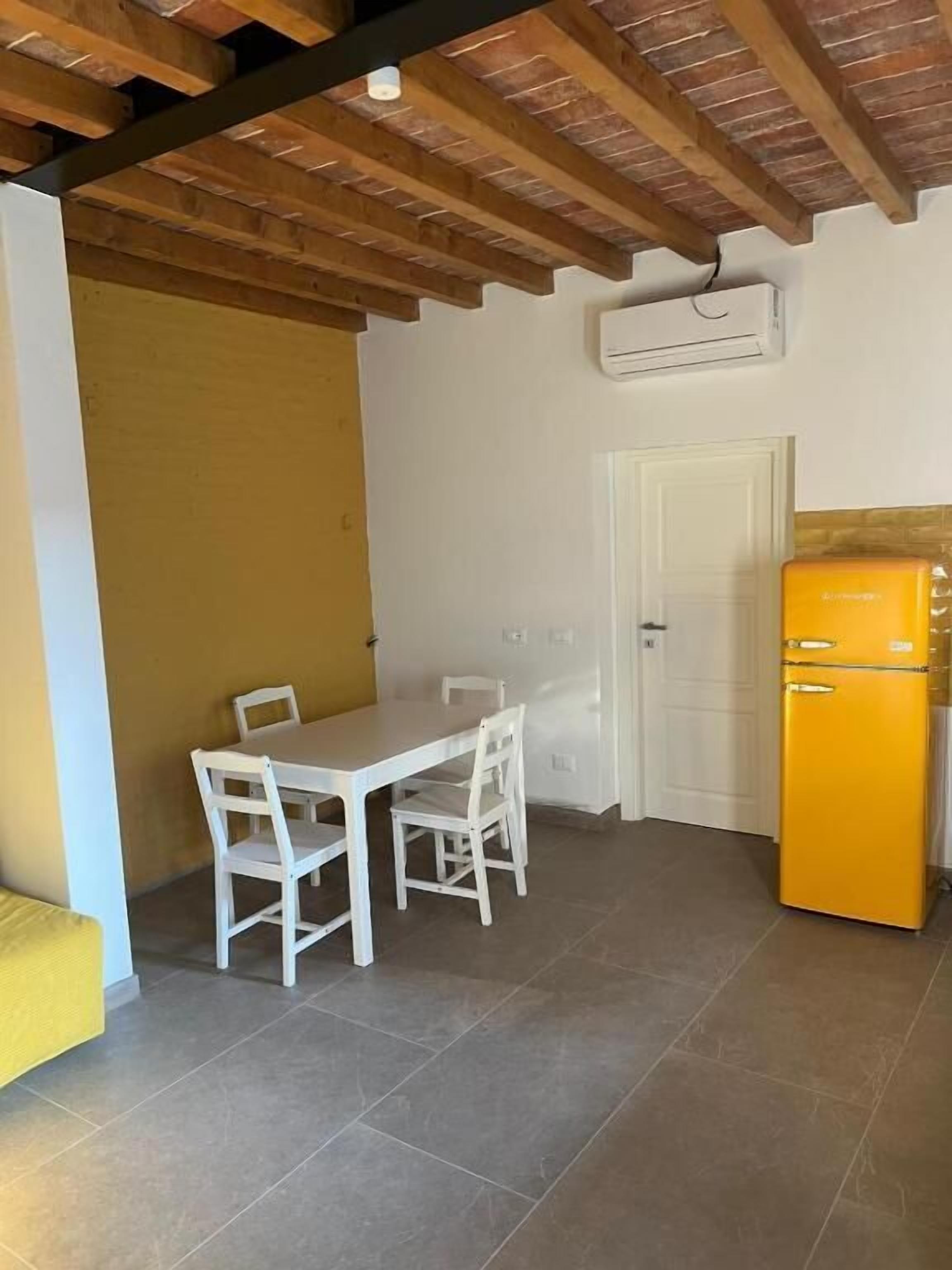 Une cuisine compacte avec une table et des chaises blanches, un réfrigérateur jaune et un plafond en bois.