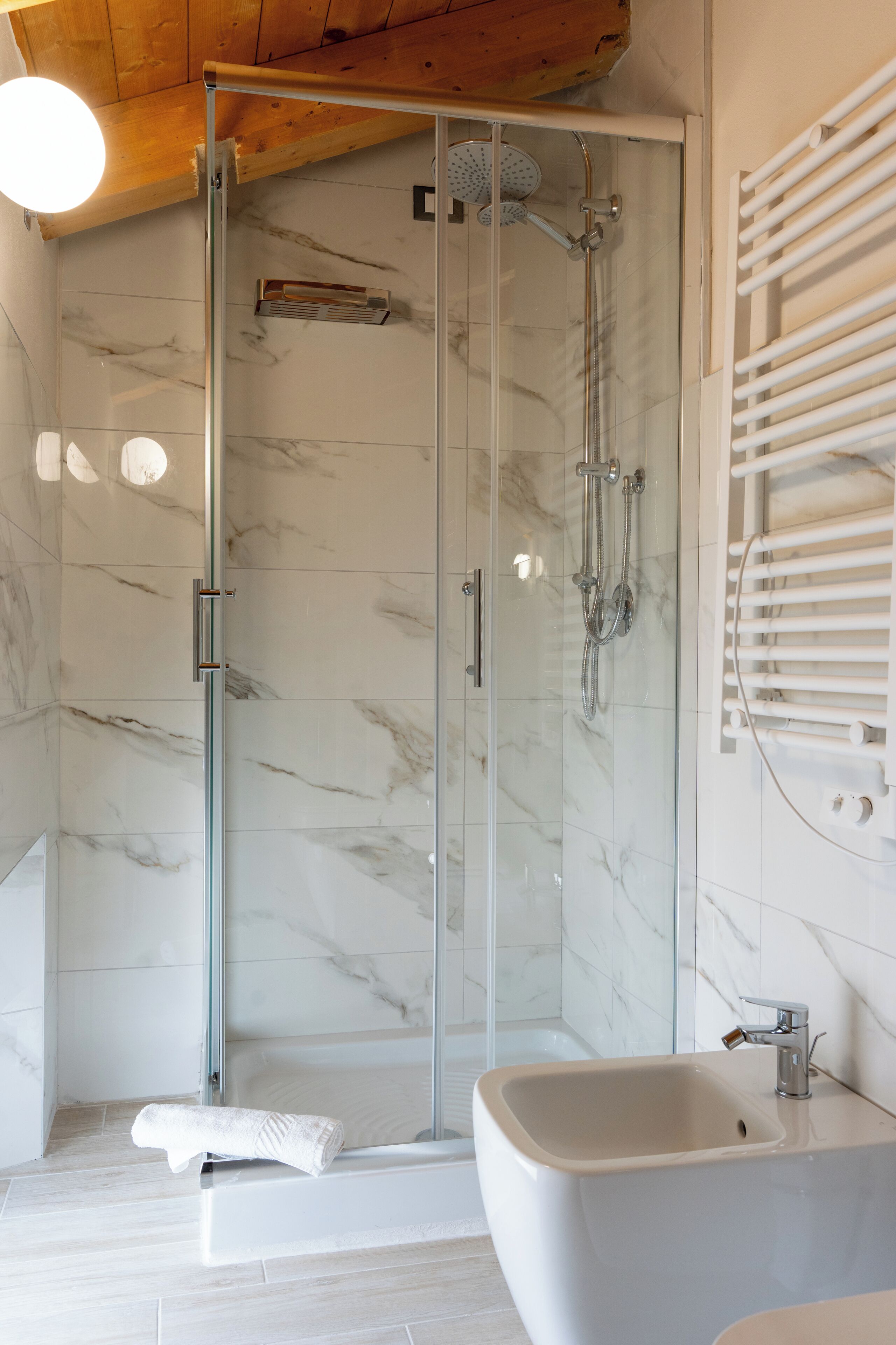 A modern bathroom with a glass-enclosed shower, a standalone bathtub, and a white towel on the floor.
