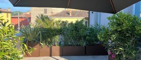 A covered patio area with a large umbrella, potted plants, and a tiled floor.