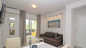 Una sala de estar moderna con sofá, una mesa de comedor con sillas, un florero con flores y un cuadro de veleros.