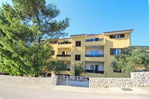 Un edificio amarillo de varios pisos con balcones, un muro de piedra y una reja de metal.