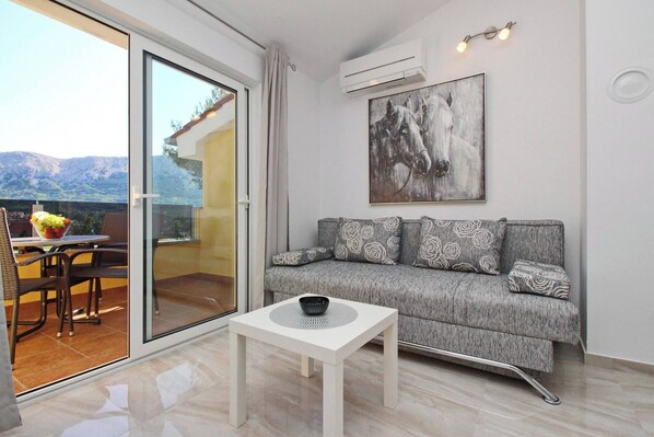 Una sala de estar moderna con un sofá gris, una mesita de centro blanca y un ventanal con vistas a un paisaje montañoso.