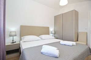 Habitación de hotel con cama, dos lámparas de noche, un armario y una toalla doblada sobre la cama.
