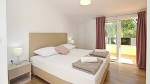 Un dormitorio con cama, lámparas de noche, mesita de noche y vista a un espacio exterior por medio de un ventanal.