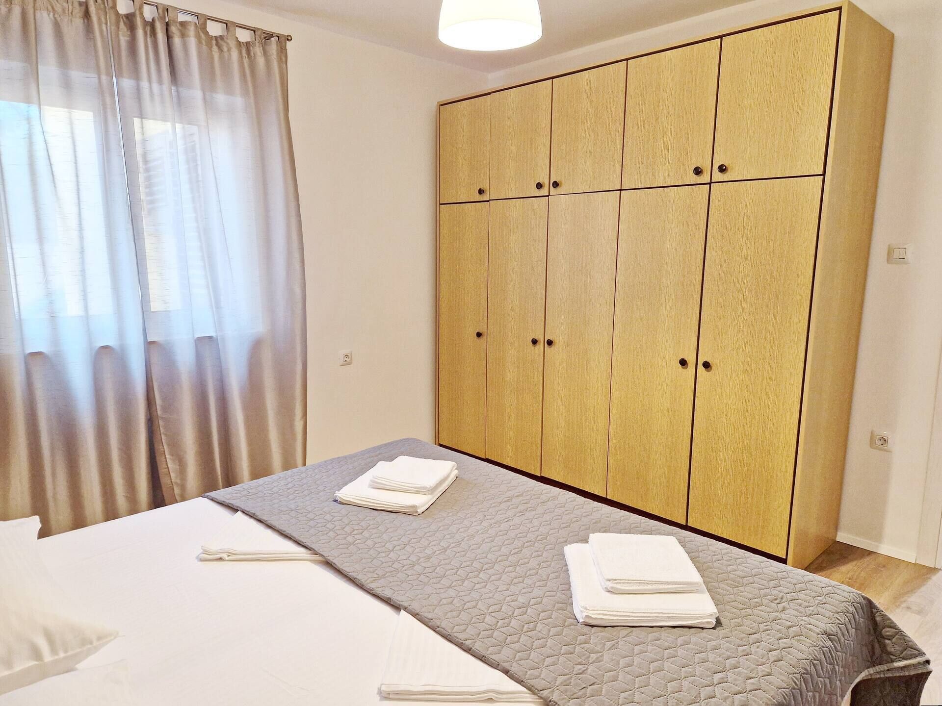 A bedroom with a bed, a grey quilted bedspread, and a large wooden wardrobe.