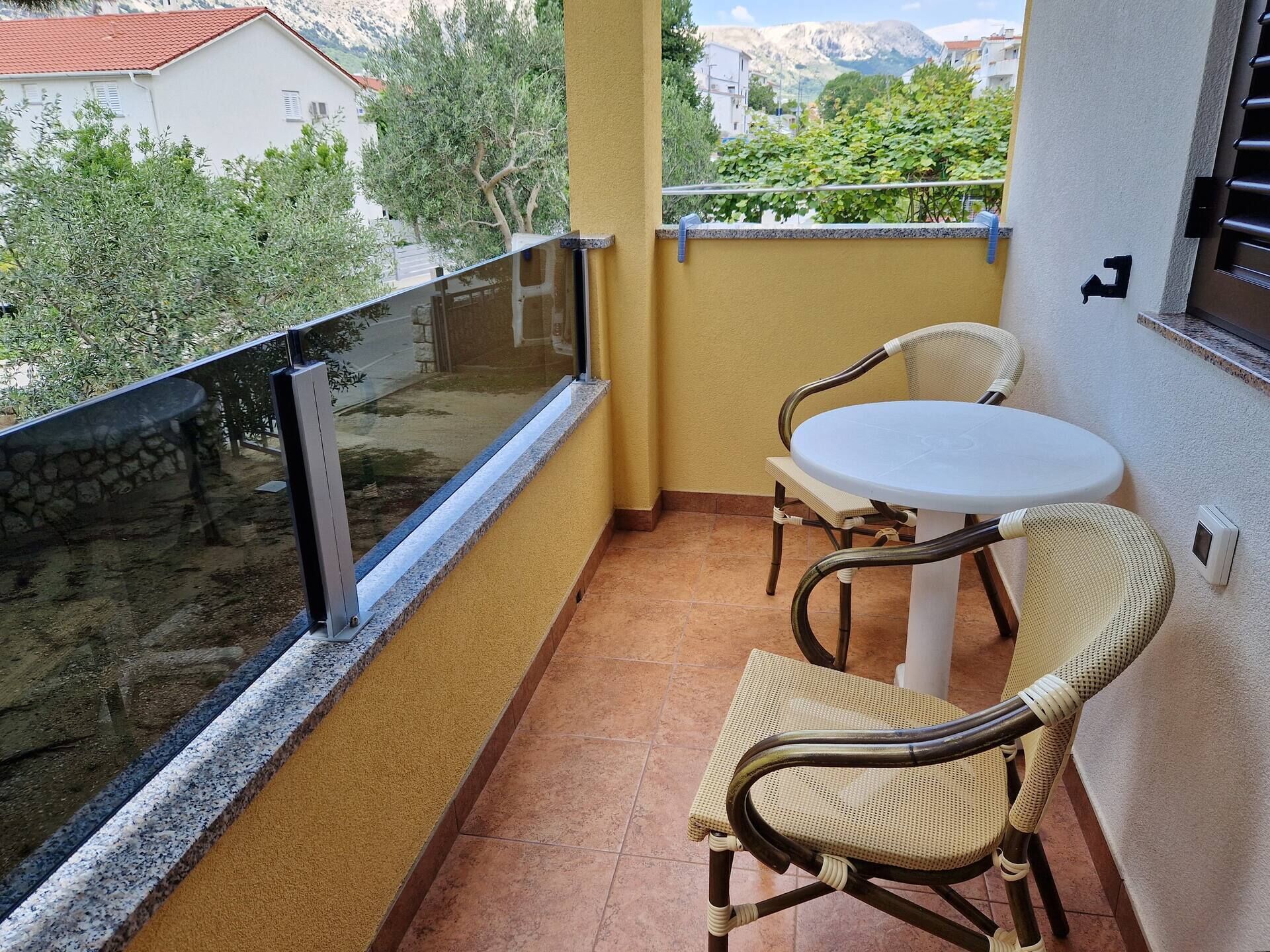 A balcony with a glass railing, a white table, and two wicker chairs.