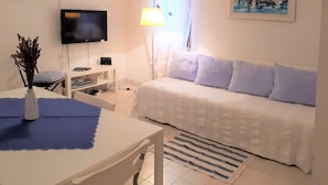 A modern, well-lit room with a white sofa, a flat-screen TV, a desk with a vase, and a painting of a harbor scene. - Apartment Valic (stari) - near the Center, 250m from the Beach (Baska)