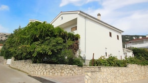 A white two-story house with a stone wall and a large tree in front. - Apartment Valic (stari) - near the Center, 250m from the Beach (Baska)