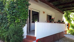 A covered outdoor area with steps leading to a white door, surrounded by greenery and potted plants. - Apartment Valic (novi) - near the Center, 250m from the Beach (Baska)