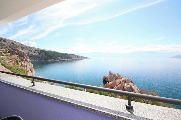 A scenic view from a balcony overlooking a calm body of water, rocky coastline, and distant mountains.