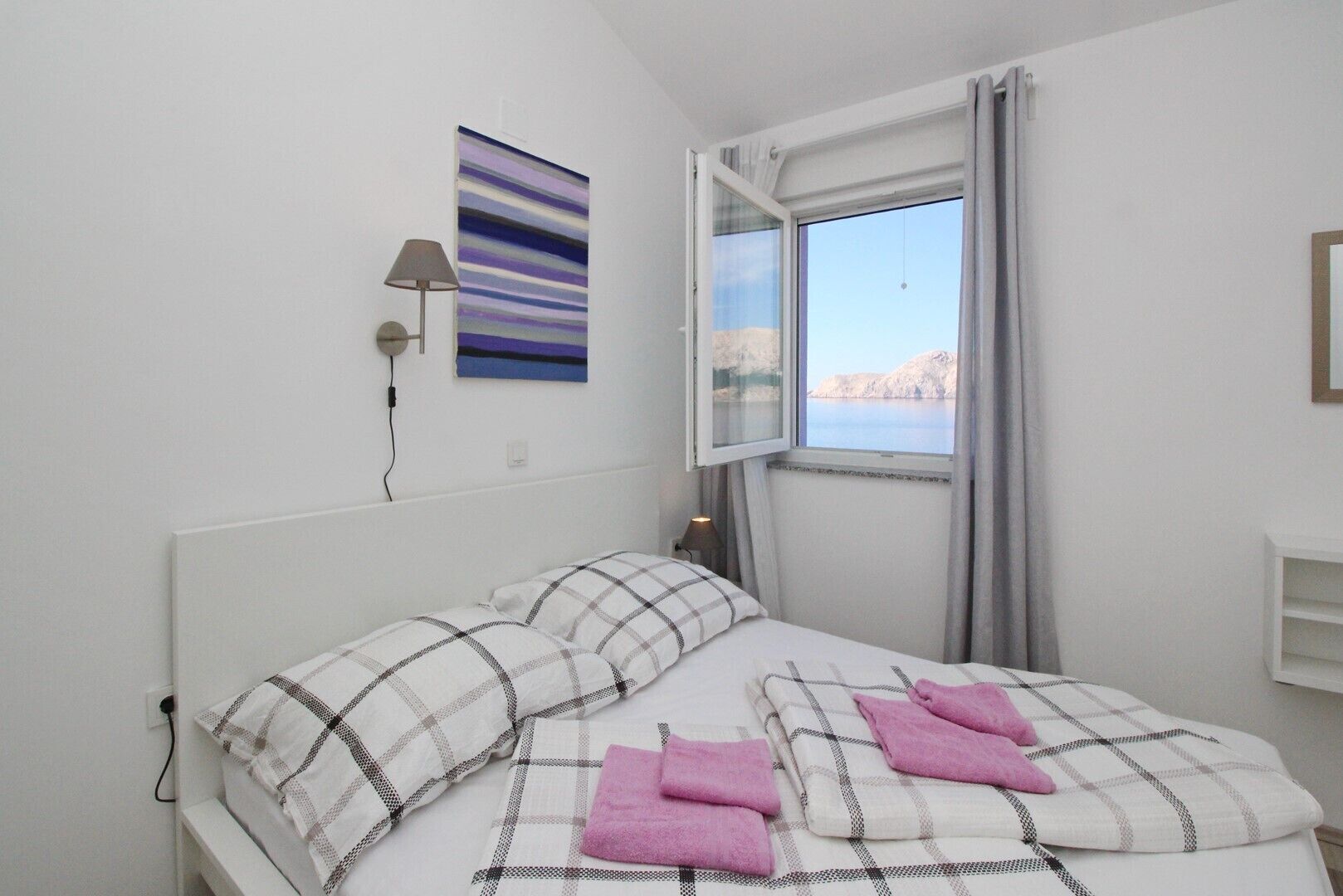 A bedroom with a bed, a window with curtains, a lamp, and a painting on the wall.