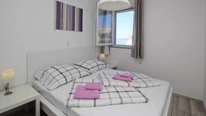 Une chambre à coucher avec un lit, des oreillers, une table de chevet avec une lampe, une fenêtre donnant sur un paysage agréable et un luminaire au plafond.