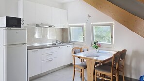 A compact kitchen with white cabinets, a microwave, and a refrigerator. There is a dining table with chairs and a vase with flowers.
