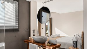 A modern bathroom with a large vessel sink, a wooden vanity, a mirror, and a bed with white linens. - Villa Altavista del Mar (Adeje)