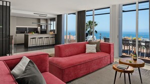A modern living room with a red sofa, a small wooden table, and a view of the ocean through large windows. - Villa Altavista del Mar (Adeje)
