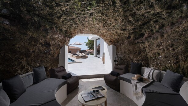 A modern interior with a circular seating area, a small table, and a view through a natural rock arch to an outdoor space with a pool and lounge chairs. - Villa Altavista del Mar (Adeje)