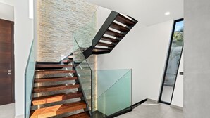 A modern staircase with glass railings and wooden steps, leading to a room with a stone wall and a door to the outside. - Atlantic Silent Heights Villa (Adeje)
